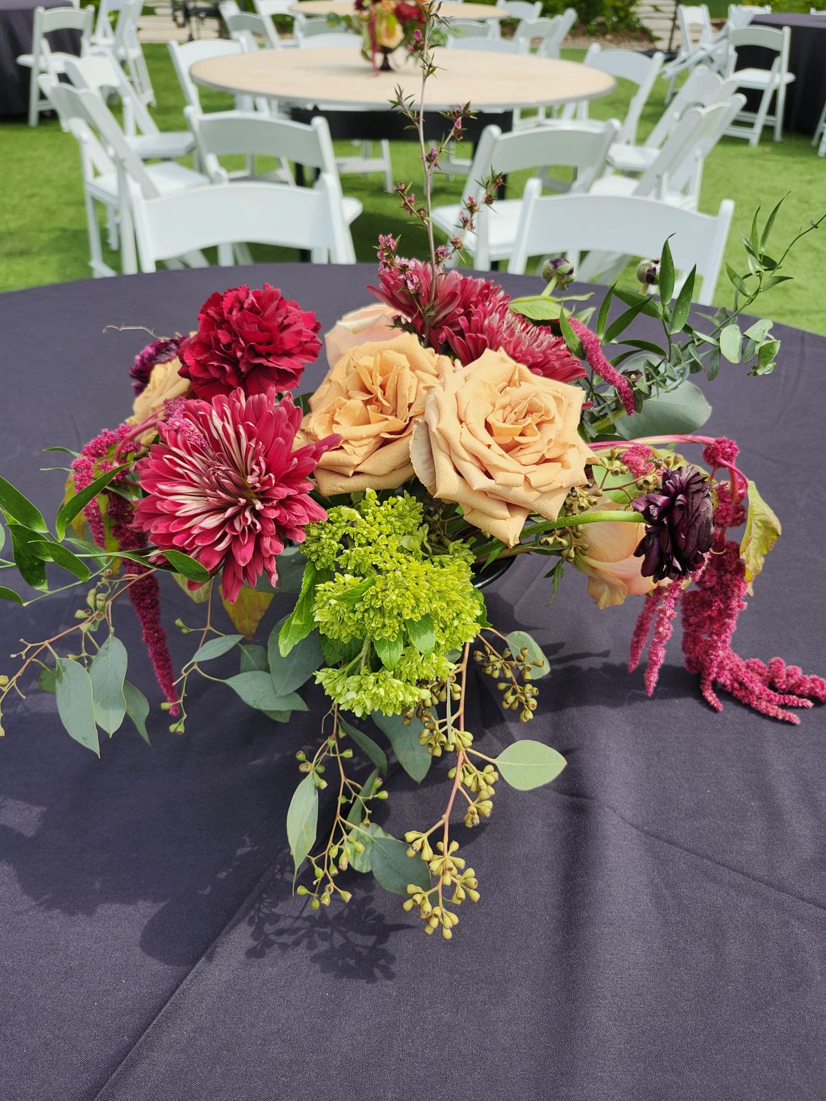Burgundy dahlia and toffee rose compote centerpiece on navy linen at an outdoor dinner